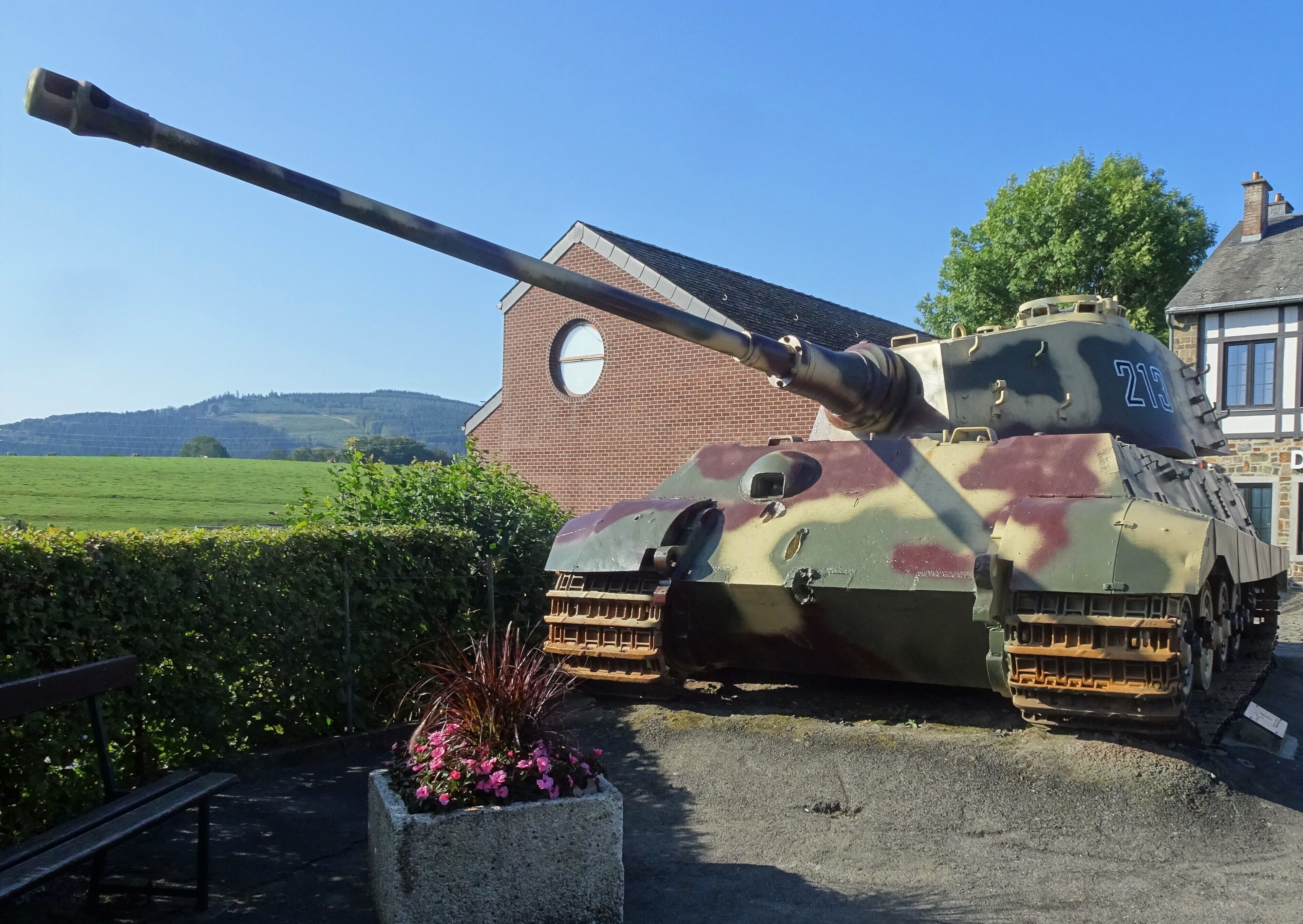 A military tank parked in front of a house with a field in the background.