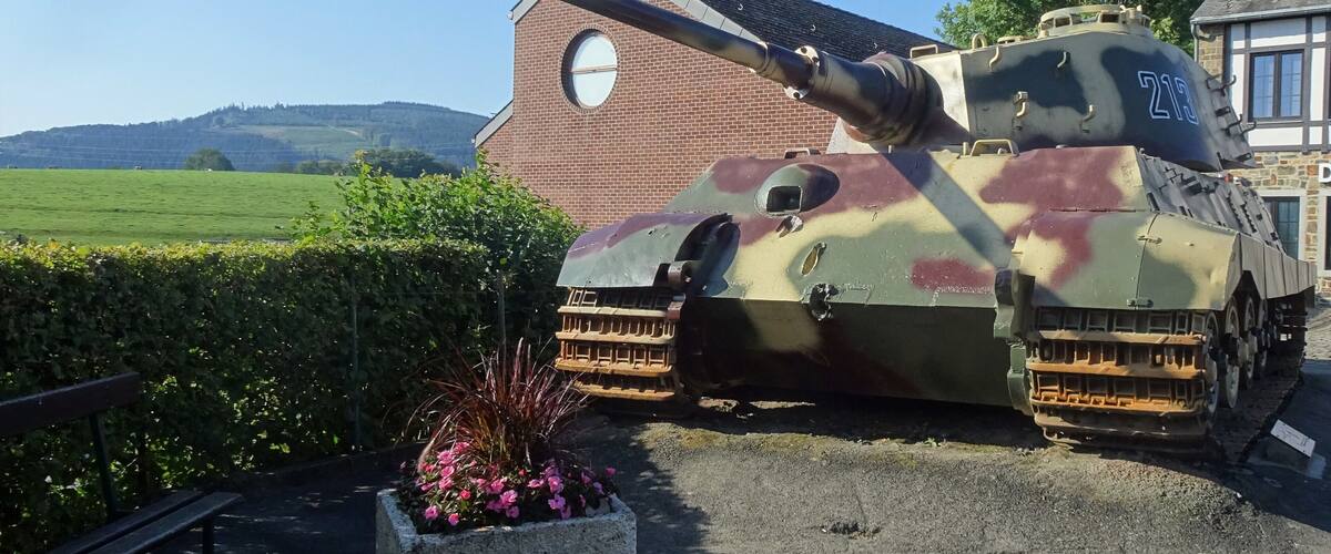 A military tank parked in front of a house with a field in the background.