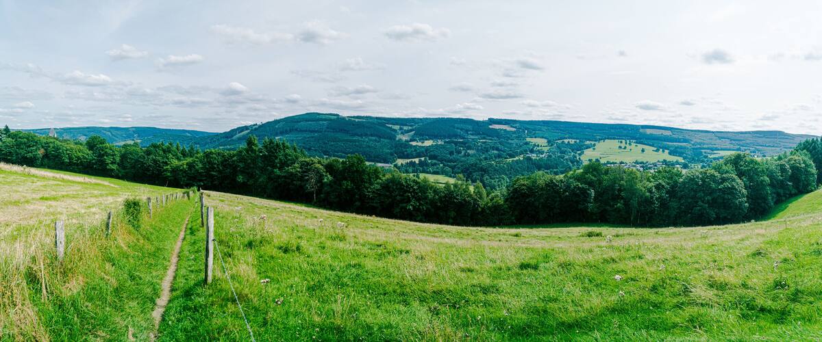 A grassy hill with a fence, a valley, and distant hills.