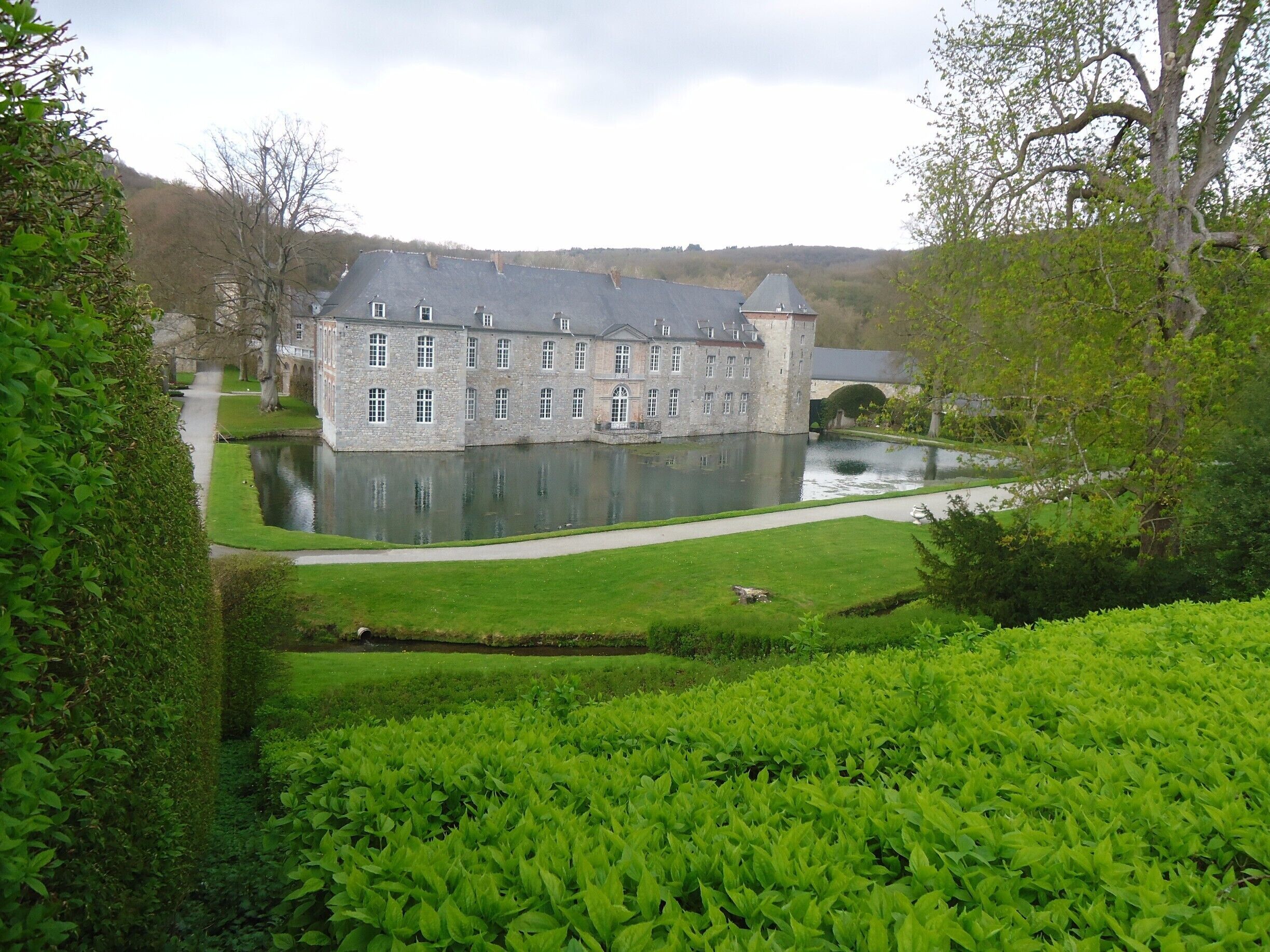 A large stone building with a reflective pond in front, surrounded by lush greenery and trees.