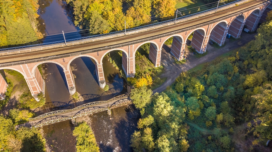 Un long pont à arches multiples enjambant une rivière, entouré d’une forêt dense.