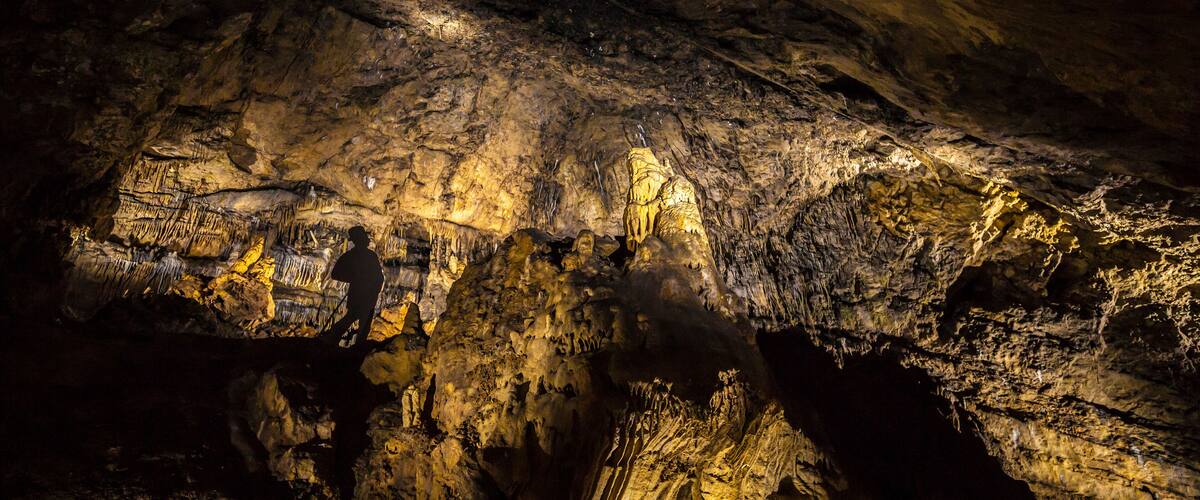 A cave with stalactites and stalagmites illuminated by artificial lighting.