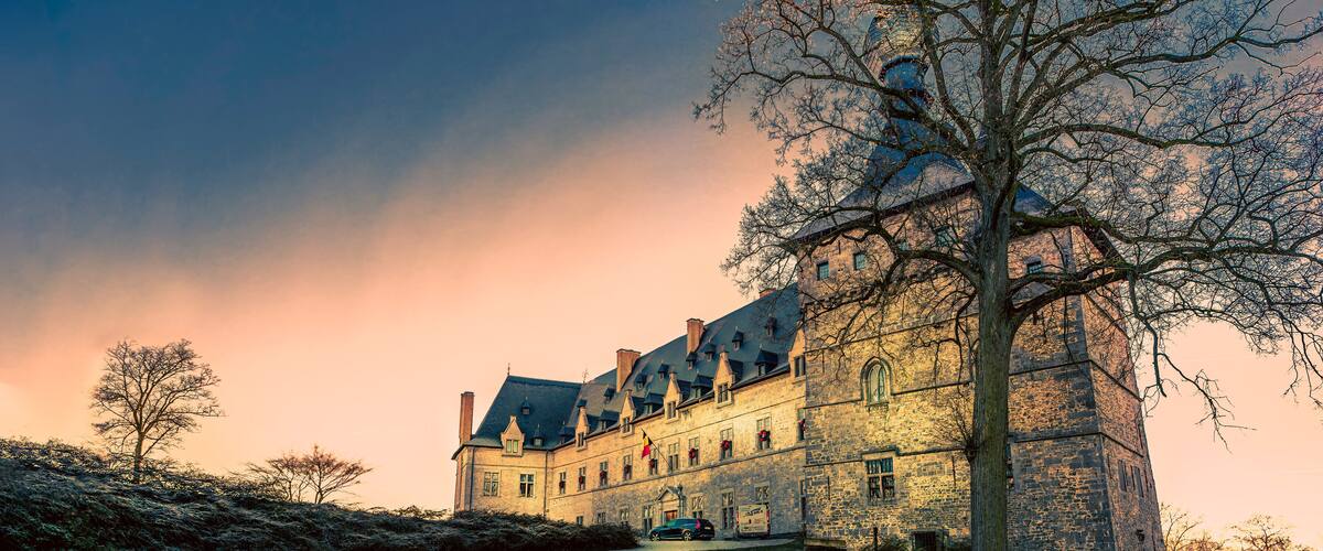 A historic stone building with a prominent tower, surrounded by trees and a cobblestone path.