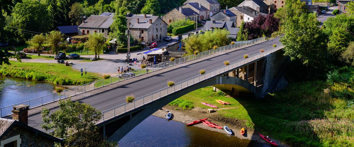 A stone bridge over a river with canoes, surrounded by houses and a church.