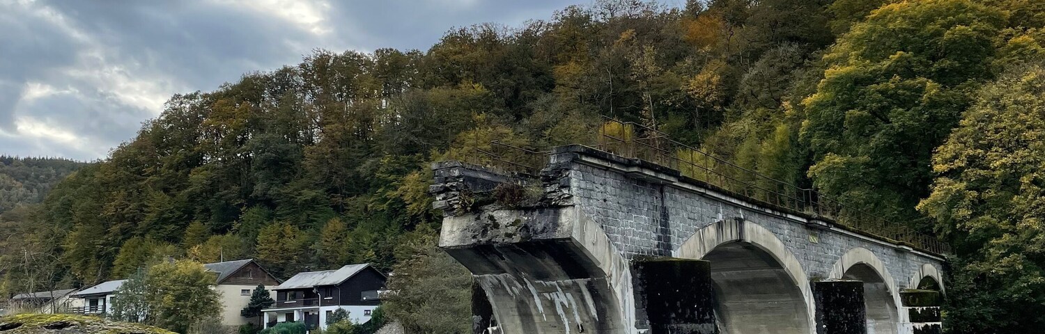 Un puente sobre un río tranquilo con un promontorio boscoso al fondo.