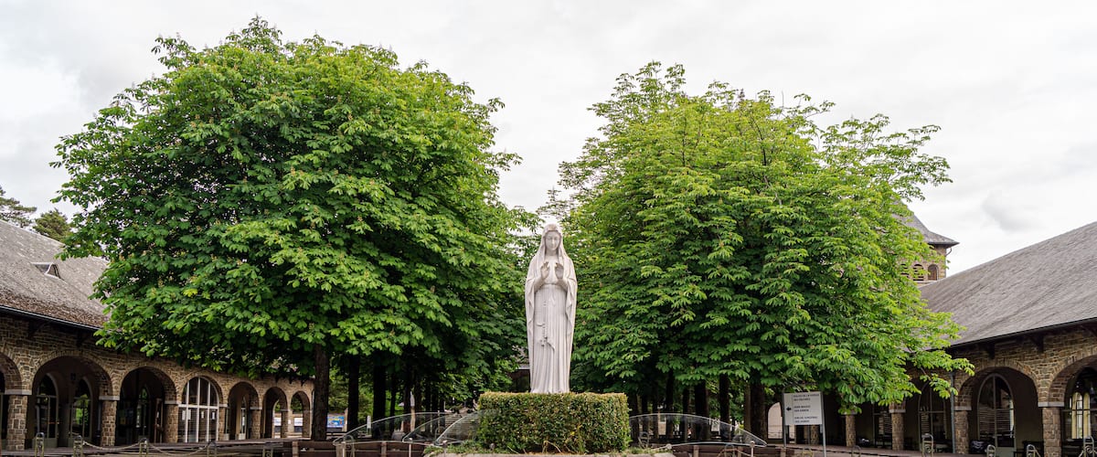 A stone monument in a courtyard surrounded by trees and historic buildings.