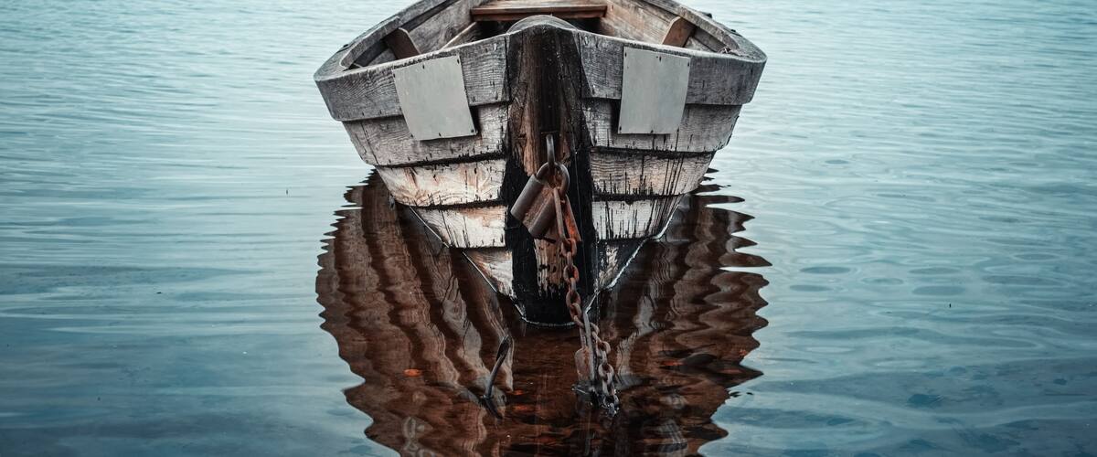 Wooden rowing boat with reflection in a still lake water at dusk.