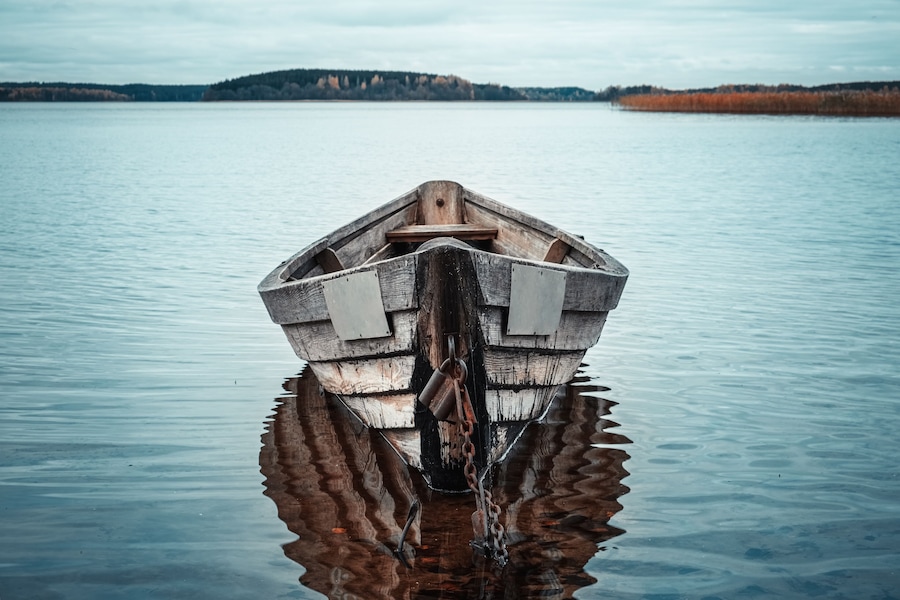 Wooden rowing boat with reflection in a still lake water at dusk.