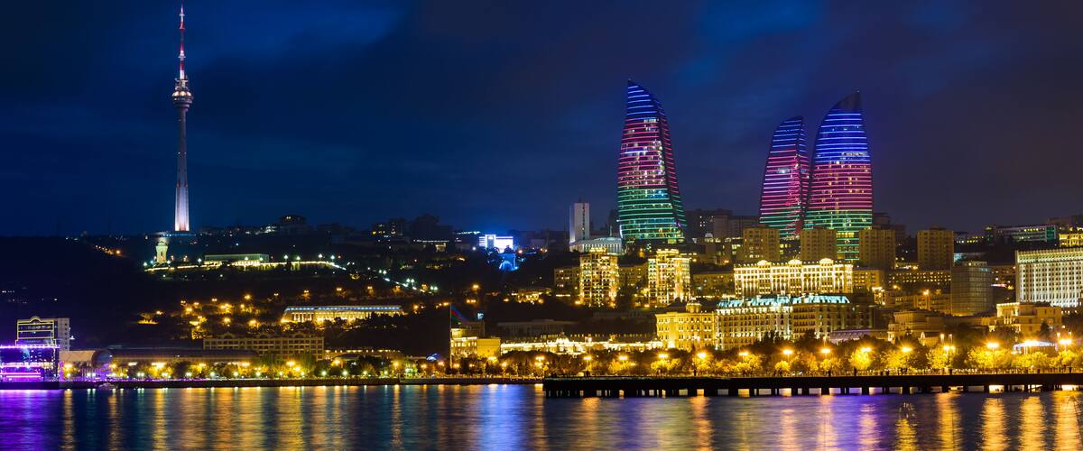 A city skyline at night with illuminated skyscrapers, a prominent tower, and a waterfront with reflections.