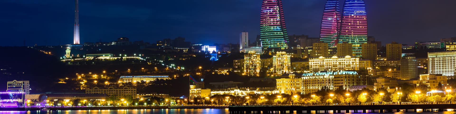 A city skyline at night with illuminated skyscrapers, a prominent tower, and a waterfront with reflections.