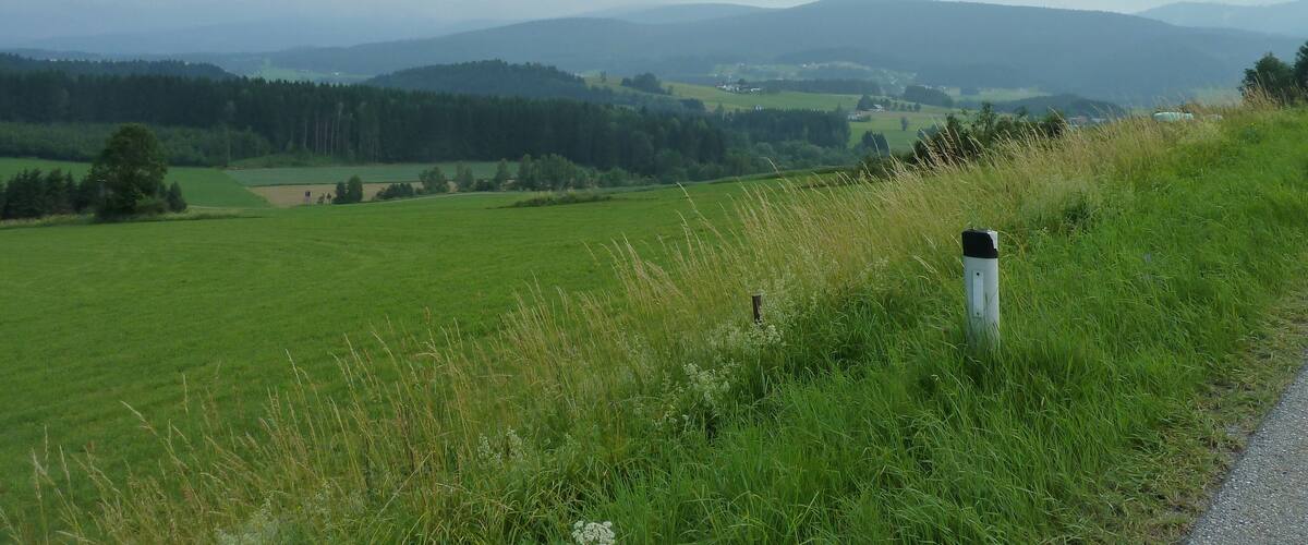 A rural landscape with rolling hills, a road, and a grassy field.