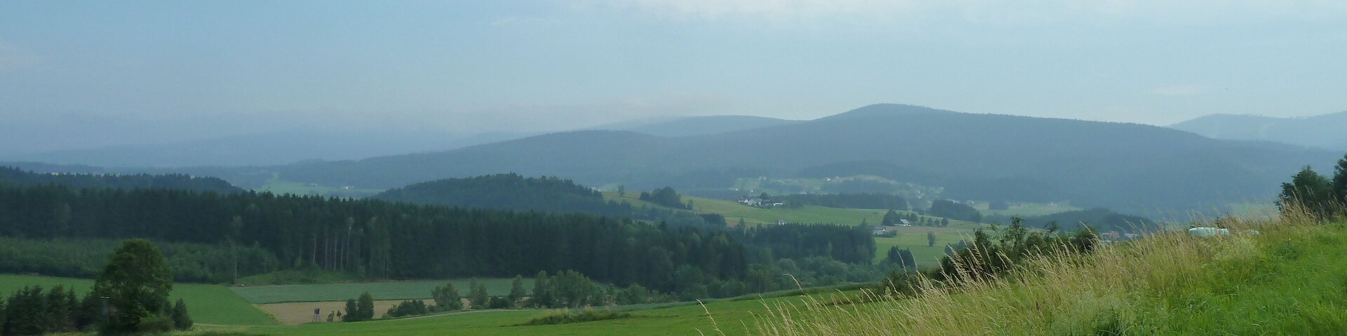 A rural landscape with rolling hills, a road, and a grassy field.