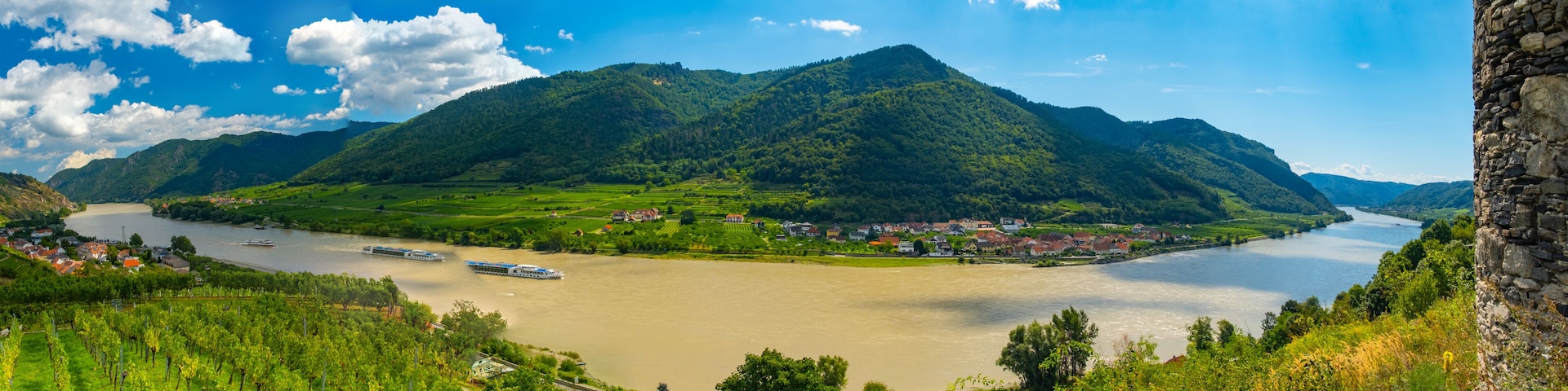 A river winding through a valley with mountains in the background and a stone tower on the right.