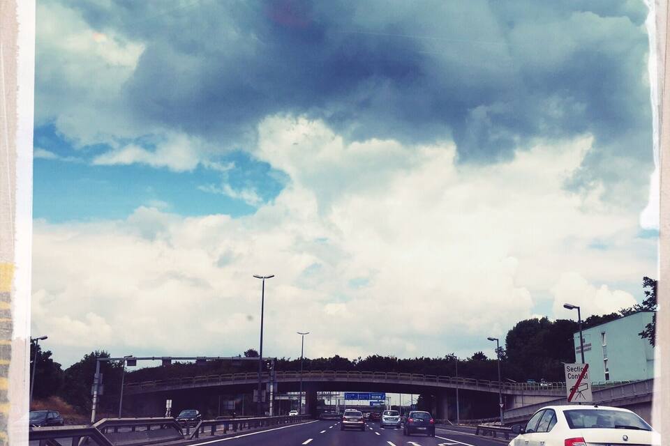 Eine mehrspurige Autobahn mit Fahrzeugen, bewölkter Himmel und einer Brücke im Hintergrund.