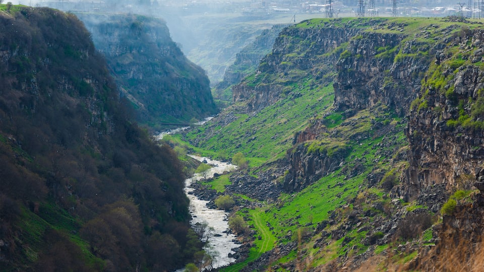 A river flowing through a valley with steep cliffs and a distant industrial area.
