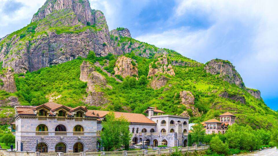 A mountainous landscape with a river, a stone bridge, and buildings with arched windows.