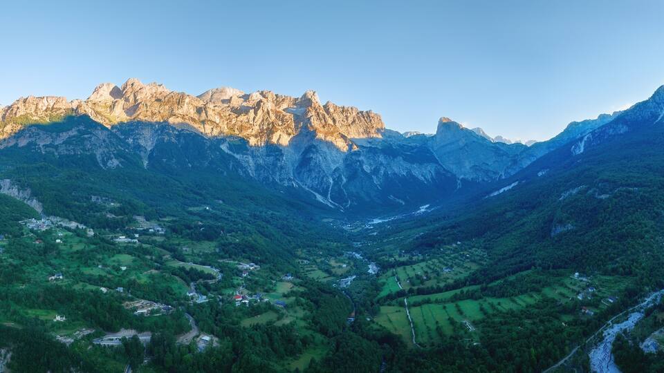 A mountainous valley with a winding river, green fields, and rocky peaks.