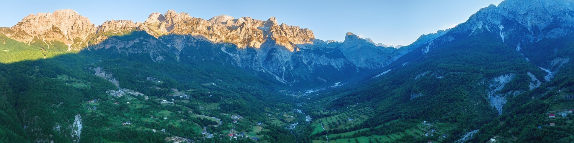 Un valle montañoso con un río sinuoso, campos verdes y cumbres rocosas.