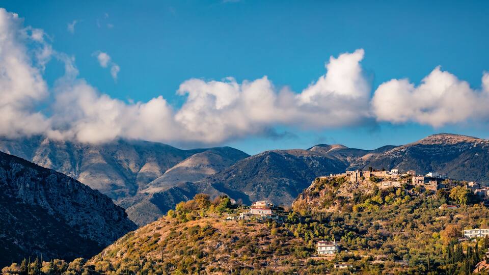 A mountainous landscape with a village on a hill, surrounded by clouds and rocky terrain.