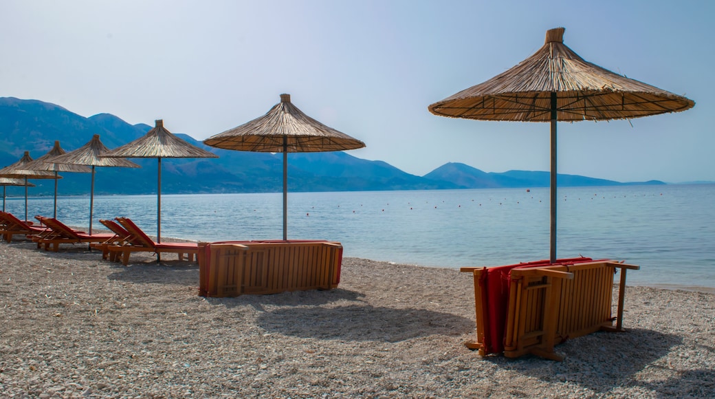 Beach umbrellas, and sun loungers on pebble beach. Qeparo village. Albania. Ionian Sea. Vacation sea concept. Summer sunny seaside landscape.