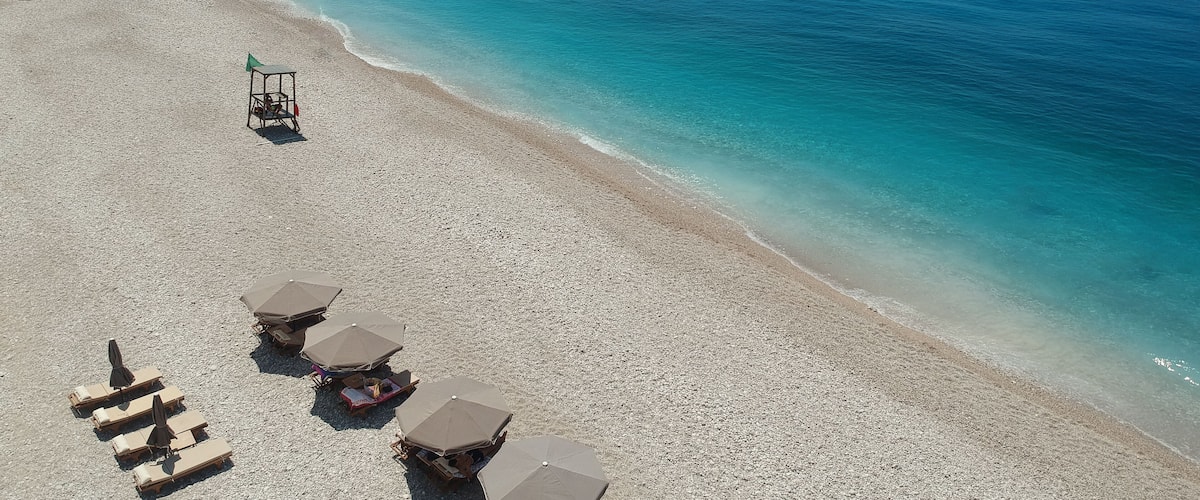 An aerial view of a pebbled beach with sun loungers and umbrellas.
