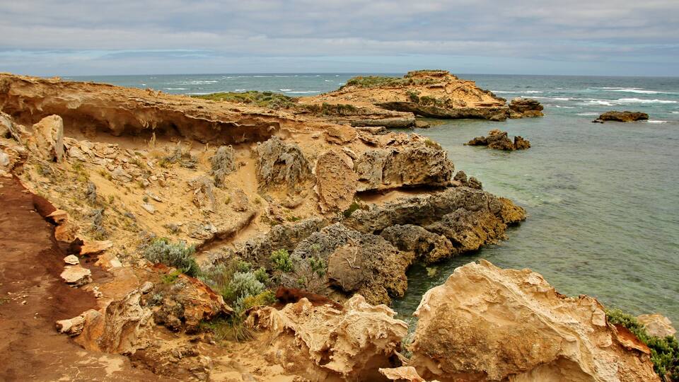 A coastal landscape with rocky cliffs, clear water, and sparse vegetation.