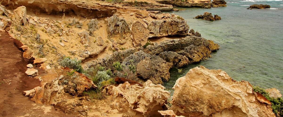 A coastal landscape with rocky cliffs, clear water, and sparse vegetation.