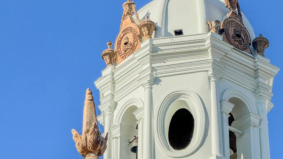 A white church with a cross on top, a bell tower, and a large circular window.