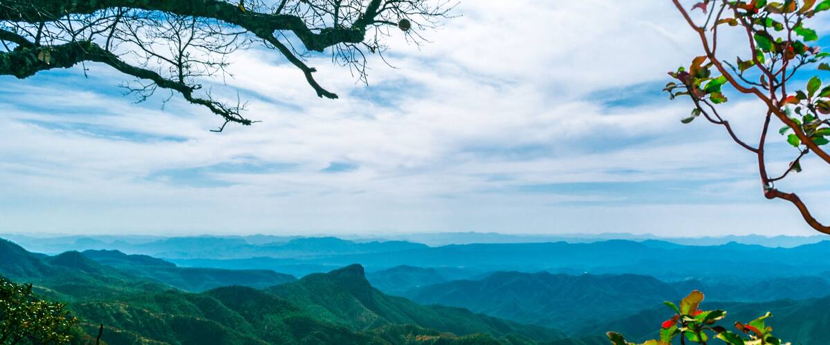 A mountainous landscape with lush greenery and distant hills under a partly cloudy sky.