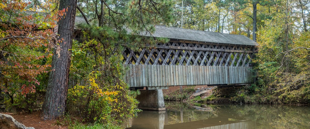 A wooden covered bridge over a calm river surrounded by autumn foliage.