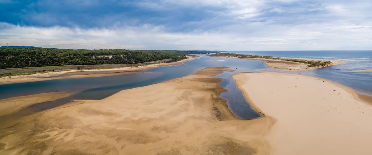 A coastal landscape with sandy beaches, a river delta, and a forested area.