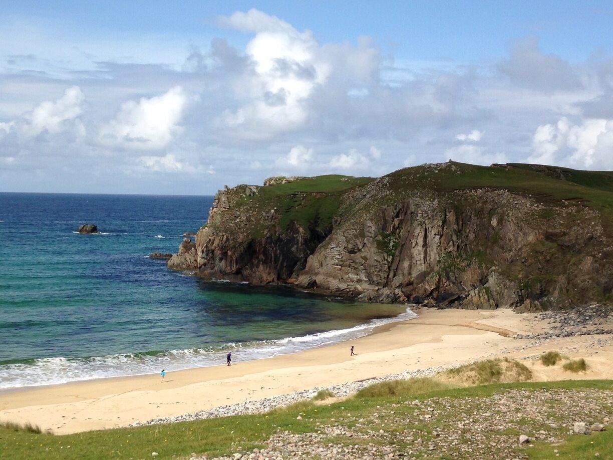 A coastal landscape with a sandy beach, rocky cliffs, and the ocean.