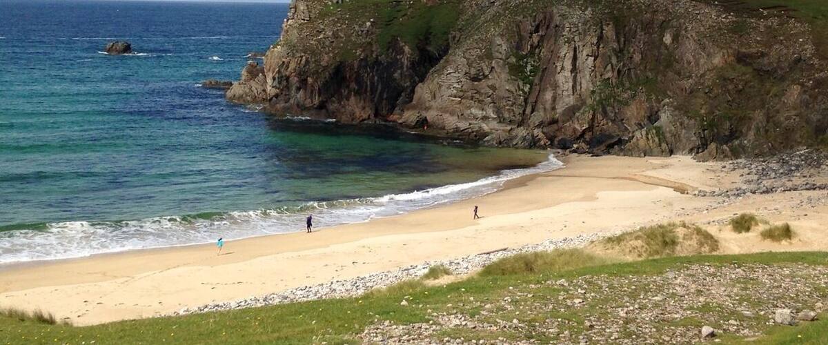 A coastal landscape with a sandy beach, rocky cliffs, and the ocean.