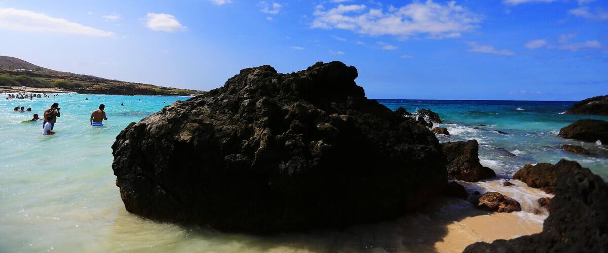 Manini'owali Beach at Kua Bay, part of Kekaha Kai State Park, is another of the very pretty Hawaii Big Island beaches, with fine white sand that slopes gently to the beautiful clear turquoise water. The swimming here is awesome when the ocean is calm, and there can be some decent snorkeling along the rocky outcroppings at either end of the beach.
During certain times of the year, particularly the summer months, the beautiful soft sand covers the entire beach from north to south. More lava rocks become exposed in the winter months as sand is carried out with the surf. Be aware of those rocks in the shallows when boogie boarding or body surfing. This is a good place to have water shoes to navigate across the rocks.
Manini'owali Beach is one of the nicer Big Island beaches that is easy to reach from Kailua-Kona. You can practically drive right to the beach, and some days it seems everyone on the Big Island knows it! If you arrive later in the day, parking can be a little crazy, especially on weekends. As you approach the beach you may see cars lined up down the road. You may have to walk down the road a bit but don't worry; there's plenty of room on the beach!
There is a rocky shoreline trail at the northern end of the beach that leads to another of our favorite Hawaii beaches, spectacular Kikaua Beach to the north. The trail winds through a lava field and across a coral beach less than a mile to scenic Kikaua Point.
