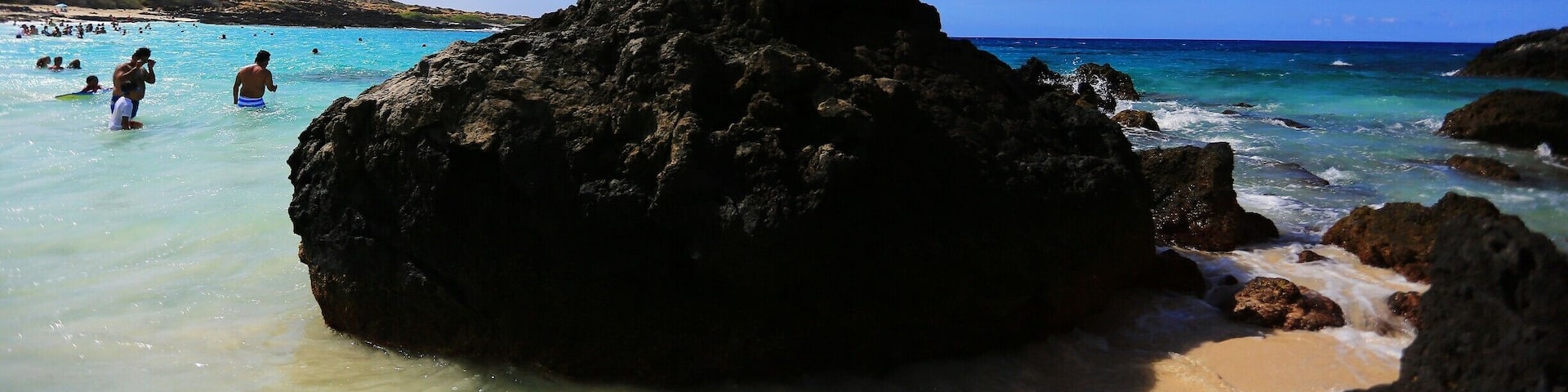 A rocky beach with clear turquoise water and a clear blue sky.