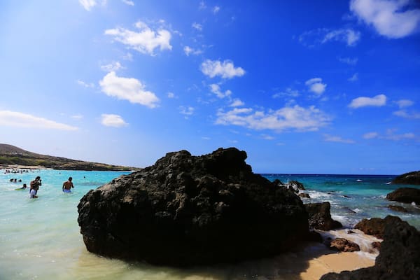 Une plage rocheuse bordée d’une eau turquoise cristalline et surplombée d’un ciel bleu azur.