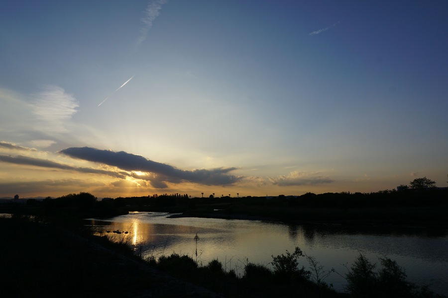 Un atardecer sobre un río con reflejos, cielo despejado y árboles distantes.