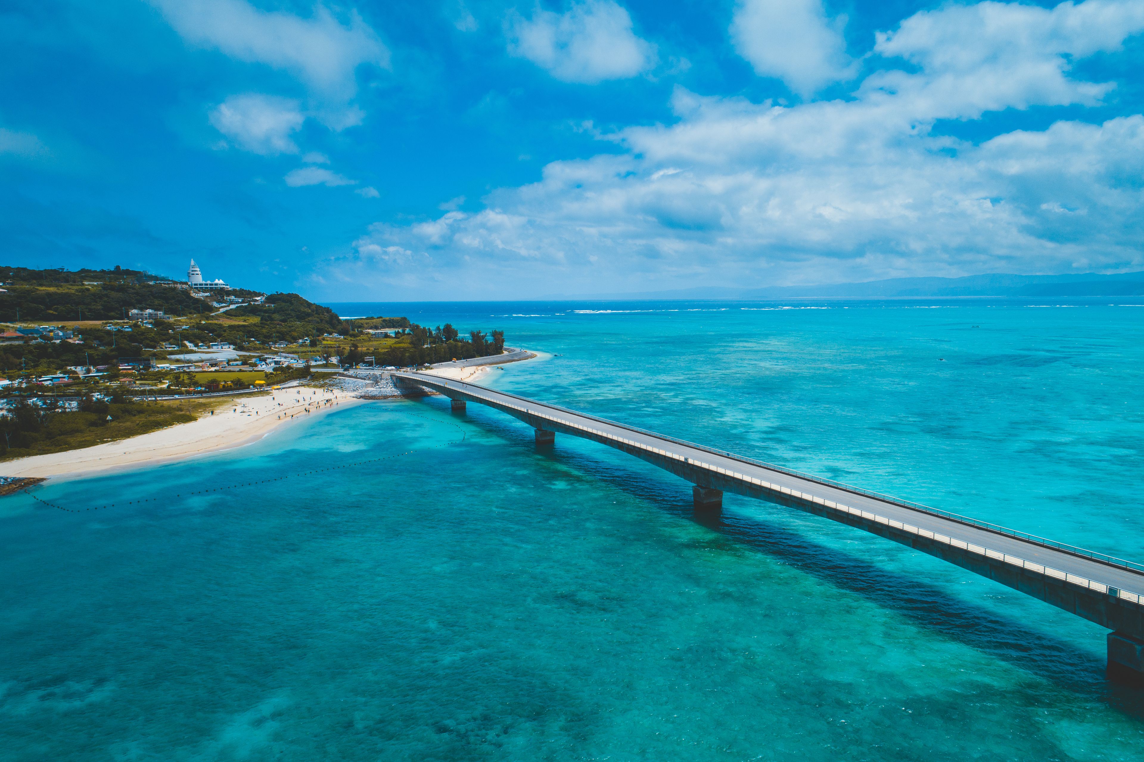 Een kustlandschap met een brug over turquoise water, een strand en een vuurtoren.