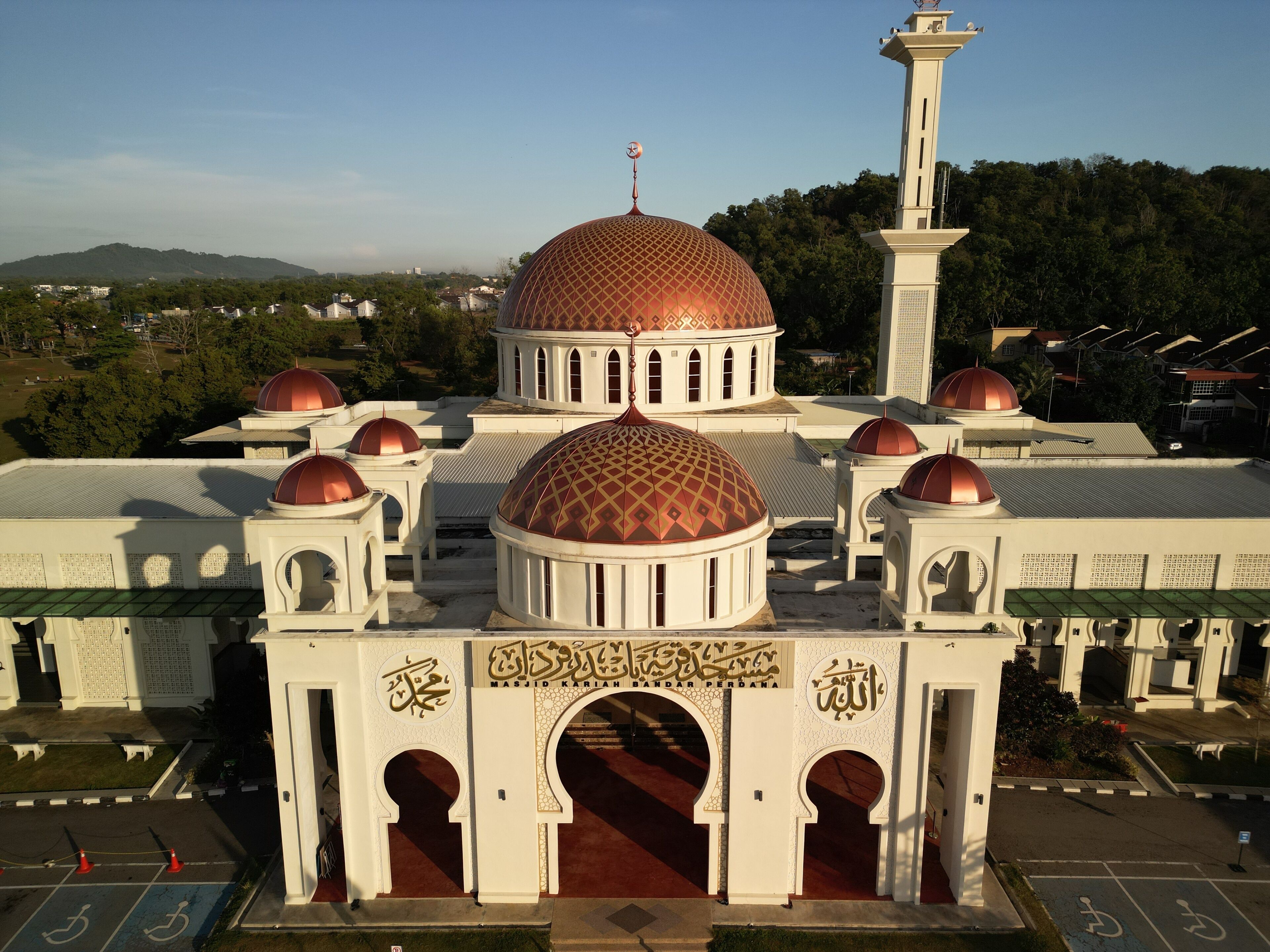 A mosque with multiple domes and minarets, surrounded by greenery and residential buildings.
