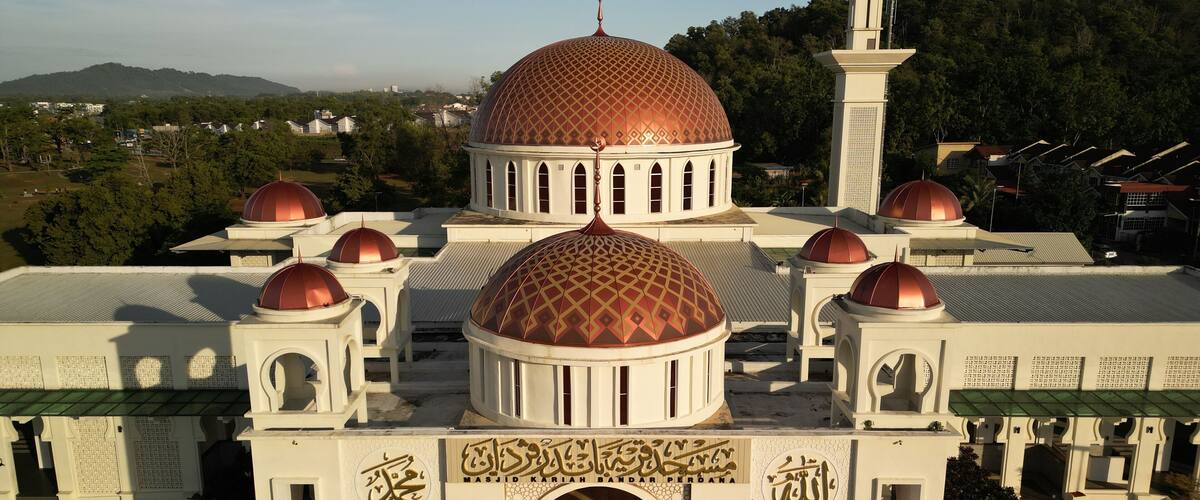 A mosque with multiple domes and minarets, surrounded by greenery and residential buildings.