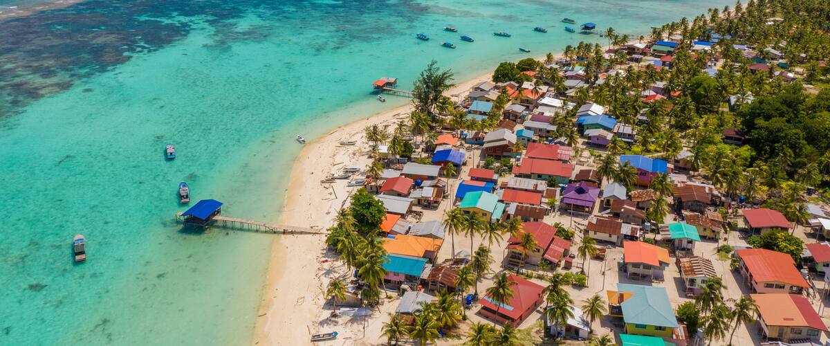 A coastal village with colorful houses, a beach, and boats in the turquoise waters.