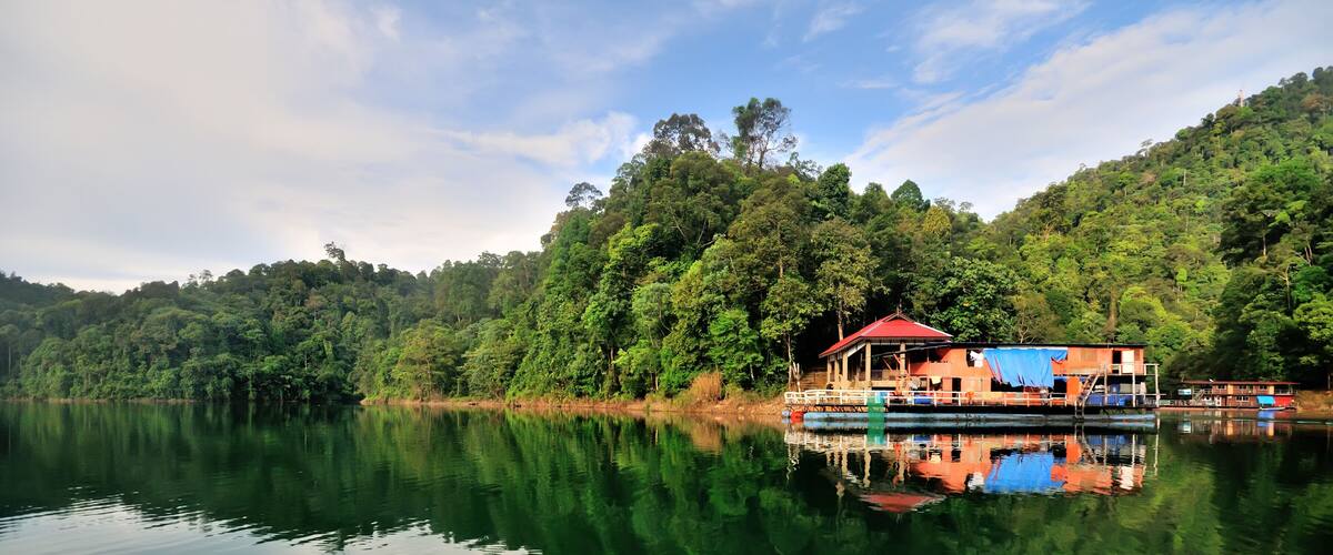 A houseboat on a calm lake surrounded by dense forest.