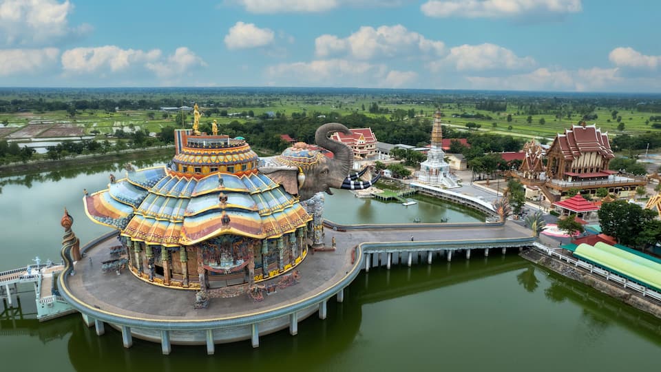 A temple complex with a large, colorful, multi-tiered roof, a large elephant statue, and a body of water.