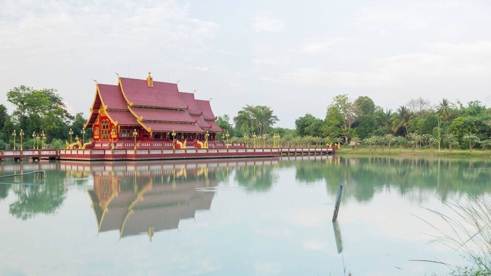 A traditional red and gold temple with a reflection in calm water.