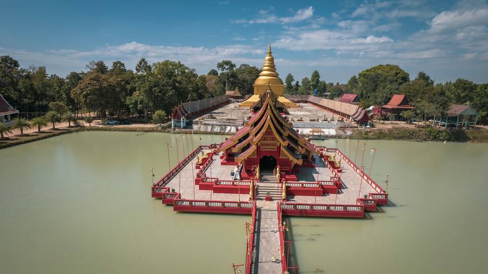 A temple with a golden spire, surrounded by a body of water and a bridge leading to it.