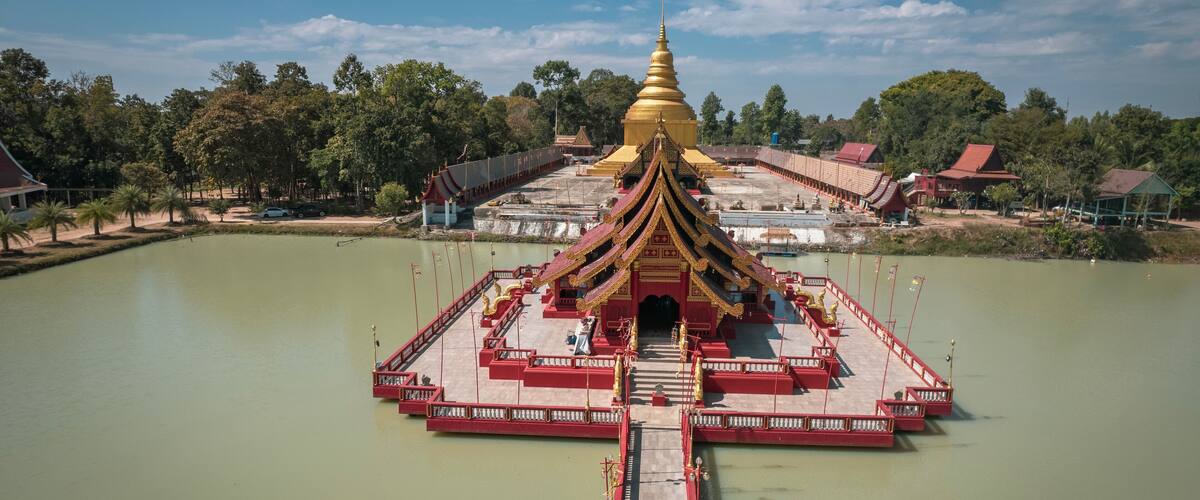 A temple with a golden spire, surrounded by a body of water and a bridge leading to it.
