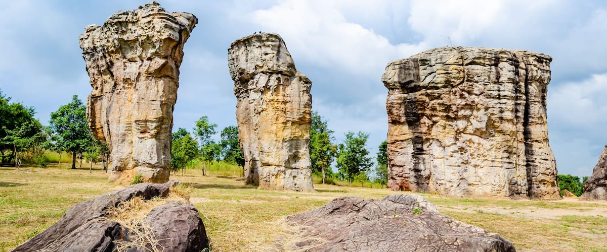 Three large rock formations in a grassy field with trees in the background.