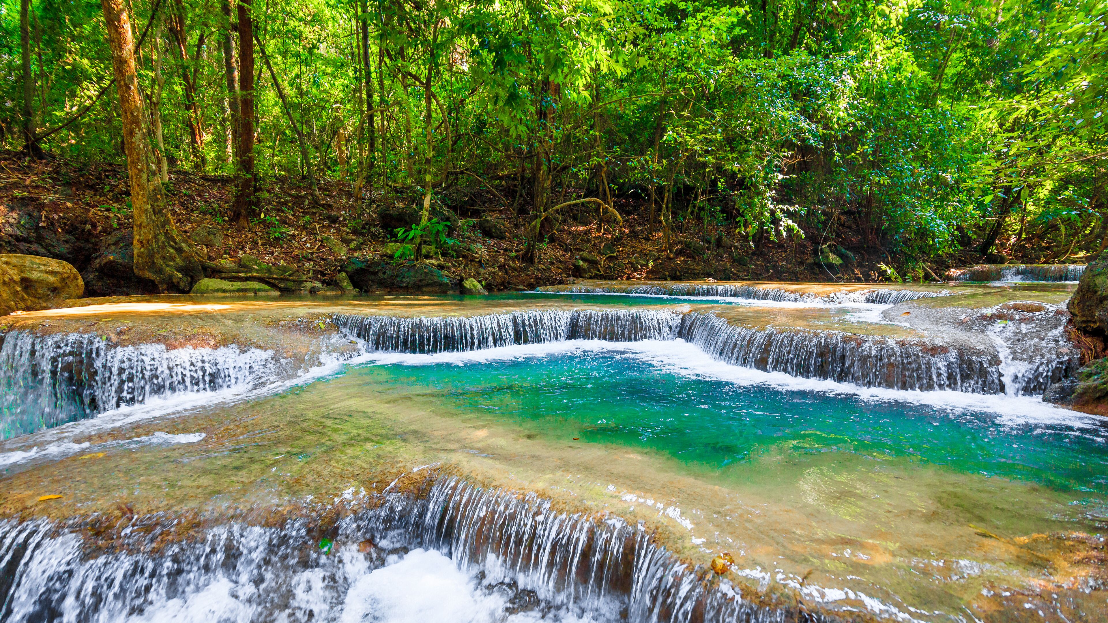 A multi-tiered waterfall in a forested area with clear turquoise water.