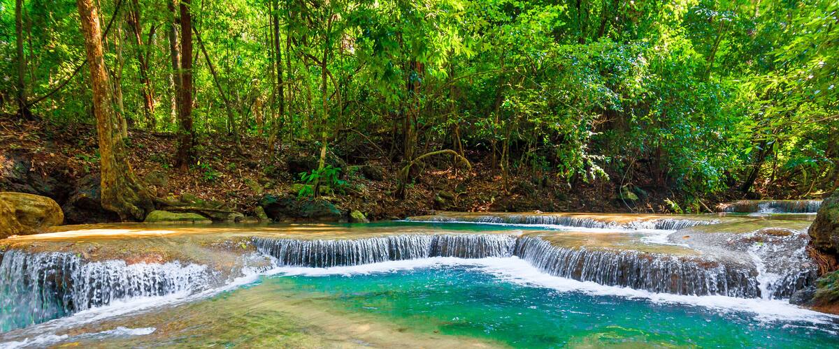 A multi-tiered waterfall in a forested area with clear turquoise water.