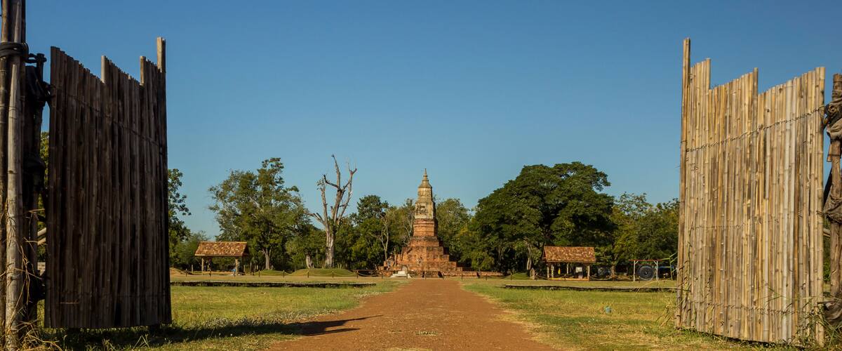 A pathway leading to a pagoda surrounded by bamboo fences and trees.